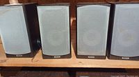 Four Tannoy Mercury MX2 speakers side by side on a shelf showing front grills and overall set.