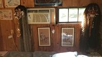 Photo showing two framed Asian wall art pieces below a window air conditioner and one large Asian wall mask mounted on wood paneling