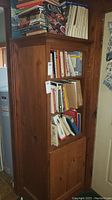 Tall pine cupboard showing three shelves with books and lower cabinet door, natural finish.