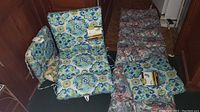 Lot showing multiple chair cushions arranged on the floor. Two distinct floral patterns visible (blue-green-white, pink-red-green) with tags on some cushions.