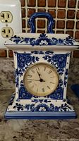 Front view of Delft Blue handpainted clock on countertop with electrical outlet in background.