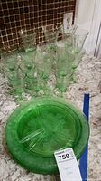 Full view of assembled green depression glassware including divided plates and stemmed glasses.