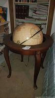 Full view of the globe on its dark wooden stand with curved legs in a room with bookshelves in the background.