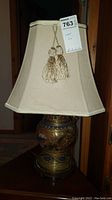 Full lamp with beige fabric shade and tassels on a wooden surface.