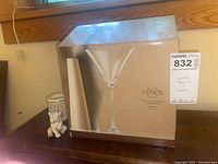 Set of four Lenox crystal martini glasses in original box alongside porcelain elephant figurine and candle holder on wooden surface.