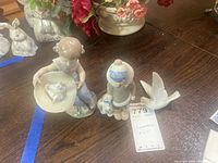 Photo showing two Lladro figurines on table — boy figurine holding hat with duck and girl figurine with duck on hat.