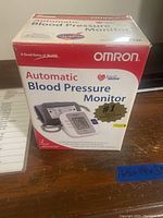Boxed Omron Automatic Blood Pressure Monitor from front showing product image and warranty information.
