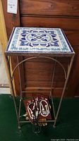 Front view of the plant table showing square mosaic tile top and metal frame with items underneath.