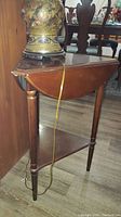 Side view of wooden triple drop leaf table with a triangular bottom shelf and one drop leaf extended. Medium brown finish with scratches visible.