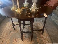 Full view of the table showing the drop leaf top partially extended with several lamp bases on top and the carved detailed legs visible underneath.