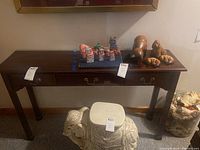 Front view of wood hall table with one drawer containing brass handles. Some objects on table surface, but table is main subject.