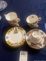 Set of stacked teacups and matching saucers showing the yellow tartan border and Scottish figure with dog pattern.