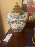 Front view of Delft Blue tobacco jar with detailed blue floral pattern and 'MARYLAND' text, on wood surface.