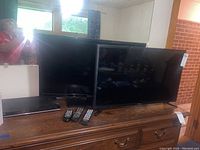 Two flat screen TVs, Samsung and Craig, along with Samsung DVD player and three remotes placed on wooden dresser.