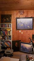 Overview photo showing all four pieces of wall art placed around a wooden paneled wall and floor area with some bookshelves and household items nearby.