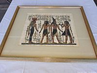Front view of framed Egyptian painting on papyrus showing four Egyptian figures and hieroglyphs.