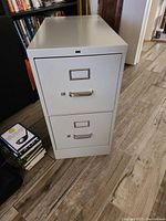 Front view of gray metal two-drawer file cabinet, showing labels, handles and locking mechanism.