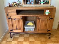 Front view of wood cabinet showing two doors with metal hinges, open shelf and cubby space below open shelf, metal legs visible