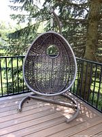 Front view of brown resin wicker egg-shaped chair suspended on metal frame on deck