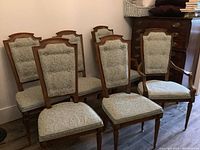 Six wood frame dining chairs grouped, showing upholstered seats, cane backs with pillows, four side chairs and two captain chairs with arms.