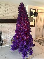 Full view of assembled purple artificial Christmas tree with red and green pre-installed lights.
