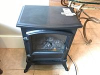 Front view of the black mini electric fireplace showing glass door with simulated logs inside and top surface with label sticker.