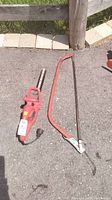 Photo showing red Homelite electric hedge trimmer and red metal frame bowsaw laying on asphalt