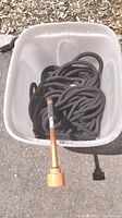 White plastic bin holding coiled black soaker and expandable hoses with a metal sprinkler wand attached to a hose.