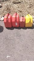 Four plastic jerry cans: two large red, one smaller red, one yellow. All without stoppers, placed on pavement.