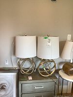 Two metal sphere base lamps with drum white cloth shades on a grey cabinet.