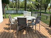 Full view of round patio table on deck with six matching sling-back metal chairs arranged around it.