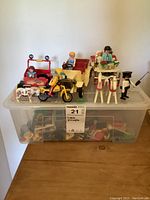 Plastic bin packed with assorted Playmobil figures and vehicles including a red car, yellow motorcycle, and several figures placed on top of the bin.