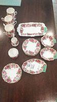 Photo showing six teacups, various plates, saucers, and serving trays with floral rose pattern and gold trim.