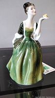 Front view showing woman seated with butterfly on fingertips, green dress and black bodice with gold accents.