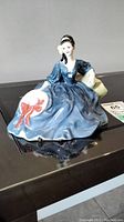 Front view of Royal Doulton 'Elyse' porcelain figurine showing the seated lady holding a white hat with a red bow.
