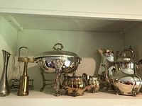 Silver plated pitcher, tea pot, cream and sugar containers, chafing dish with legs and lid, bud vase, rack, brass corkscrew arranged on shelf.