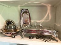 Silver plate chafing dish stand with lid, serving tray, small silver ring, wine coaster bowl, forks, and small dish displayed on shelf.