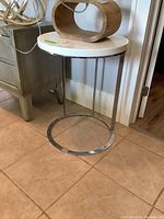 Full view of small round side table with white top and chrome metal base, showing its height and placement in room.