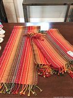 Table runner and placemats laid on a wooden table showing striped fall colors and twisted fringe ends.
