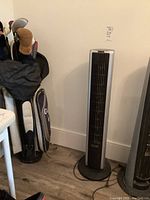 Front view of the black tower fan standing upright next to golf bags and a chair.