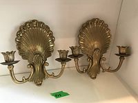 Pair of brass wall sconces with shell-shaped backplates and two candleholders each, shown side by side on a white surface.