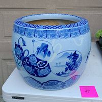 Front angle of the large blue and white pot showing detailed Asian motifs and overall shape on a white table.