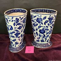 Front view of two large blue and white flowered vases side by side on a dark cloth background with lot number card in front.