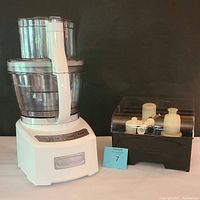 Full front view of Cuisinart food processor with main 12 cup bowl attached and clear additional bowls and attachment storage box beside it.