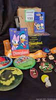 Lot of assorted Disneyana memorabilia items including pins, buttons, lanyard, luggage tag, and commemorative bulb box on black cloth background