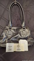 Front view of black leather handbag with double straps, showing the attached tags and receipt beneath the bag.