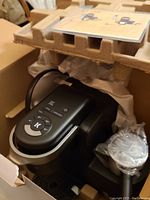 Machine base and control panel with frother cup visible inside inner packaging.