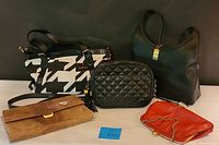 Five handbags displayed on white surface against dark background showing variety and condition.