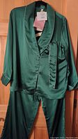 Emerald green silk pajama top and pants hanging on a hanger, showing front details and tags.