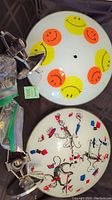 Photo showing both glass light fixtures side by side, one decorated with colorful smiley faces and the other with Dr. Seuss characters. Includes metal hardware components and plastic bags with accessory parts visible.